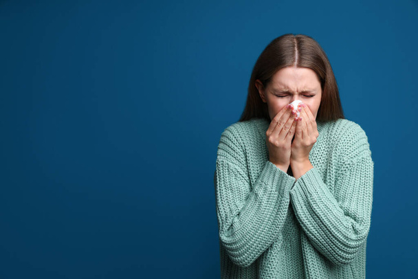 Young woman sneezing on blue background, space for text. Cold symptoms - Foto, Bild
