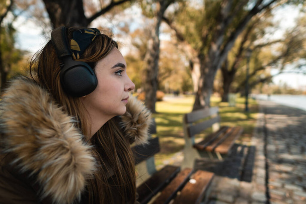 Una mujer bastante caucásica escuchando música en el parque y mirando a un lado. Copiar espacio - Foto, Imagen