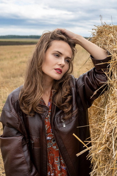 girl in a leather jacket stands in a field by a stack of straw - Photo, Image