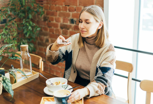 Mujer joven en traje casual toma fotos de comida en el teléfono inteligente en la cafetería  - Foto, imagen