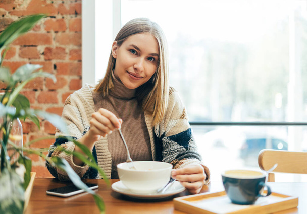 Jonge lachende blonde vrouw in casual kleding lunchen in het cafe - Foto, afbeelding