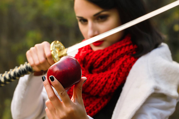 Eine Frau mit scharfer Klinge in den Händen ist dabei, einen roten Apfel zu schneiden. - Foto, Bild