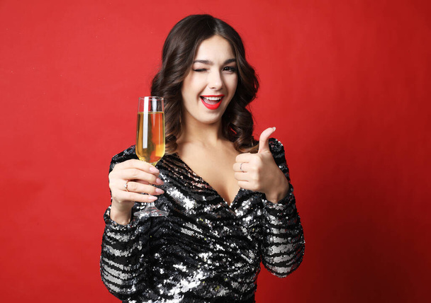 woman in black evening dress holding glass of champagne over red background - Фото, зображення