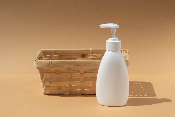 wicker basket and white dispenser bottle, for spa cosmetic products on a beige background. - Foto, immagini