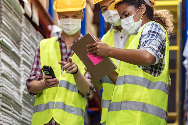 Interracial team Asian African Caucasian working on inventory use barcode scanner and digital tablet in distribution center. They wear face mask prevent from COVID-19. Warehouse and hygiene concept. - Foto, Imagem