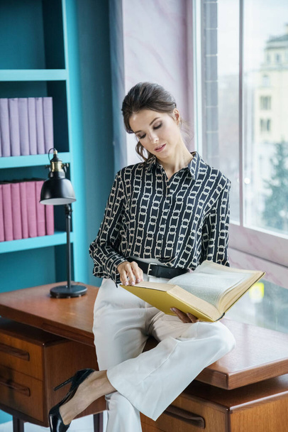 Beautiful young woman posing at home library interior. Portrait of beauty brunette in casual clothes  - Foto, afbeelding