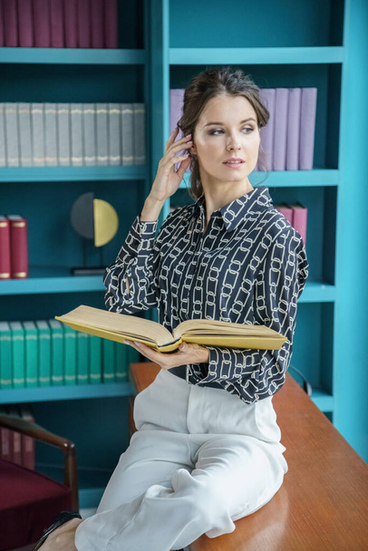 Beautiful young woman posing at home library interior. Portrait of beauty brunette in casual clothes  - 写真・画像