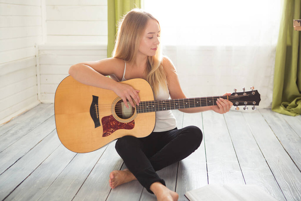Attractive woman with guitar sitting in light room with wooden floor. Musician, concert, hobby, leisure, rehearsal concept - Foto, imagen