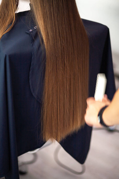 Парикмахер стилист расчесывает длинные светлые волосы в салоне красоты, уход за волосами. - Фото, изображение