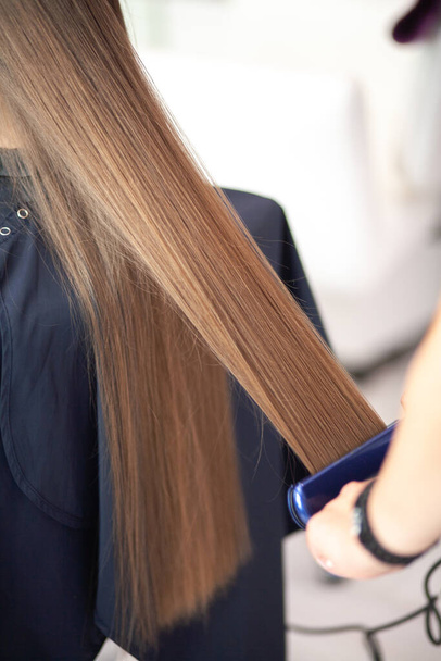 Peluquería estilista peinando pelo largo y rubio en un salón de belleza, cuidado del cabello. - Foto, Imagen