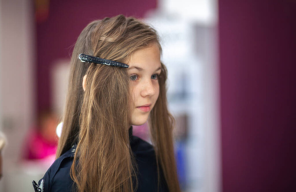 Hermosa joven europea se sienta en un salón de belleza, peluquero profesional estilista trabaja con el pelo largo de una chica. - Foto, imagen