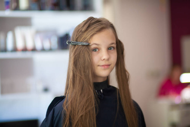 Красивая молодая европейская девушка сидит в салоне красоты, профессиональный парикмахер стилист работает с длинными волосами девушки. - Фото, изображение