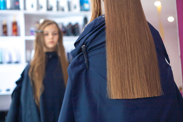 Menina europeia jovem bonita senta-se em um salão de beleza, cabeleireiro profissional stylist trabalha com cabelos longos de uma menina. - Foto, Imagem