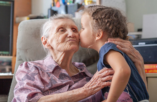 De kleindochter kust haar overgrootmoeder in het erts, tedere relaties, liefde voor geliefden, familiewaarden. - Foto, afbeelding