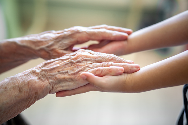 De handen van het kind in de handen van de grootmoeder, de oude bruinachtige huid bij de oudere vrouw, moederlijke liefde en zorg. - Foto, afbeelding