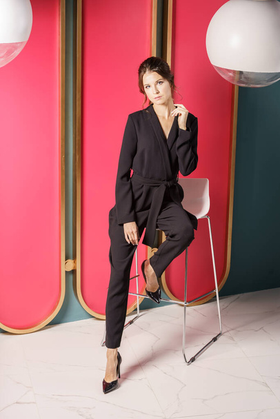 Beautiful businesswoman standing close to red wall at luxury apartments interior. Portrait of beauty brunette in black suit and high heels  - Fotó, kép