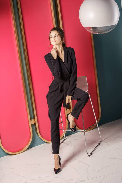 Beautiful businesswoman standing close to red wall at luxury apartments interior. Portrait of beauty brunette in black suit and high heels  - 写真・画像