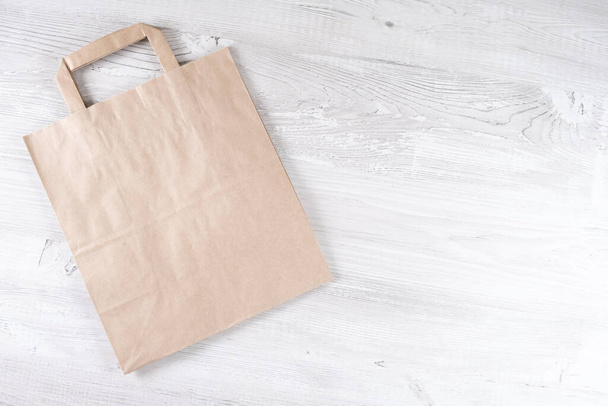 Brown eco paper bag on a white wooden table. Place for your logo. - Photo, image