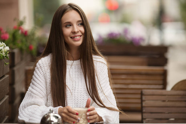 Fiatal, gyönyörű, csinos nő mosolyog egy kávézóban, kezében egy bögre kávéval. Másolás-páz - Fotó, kép