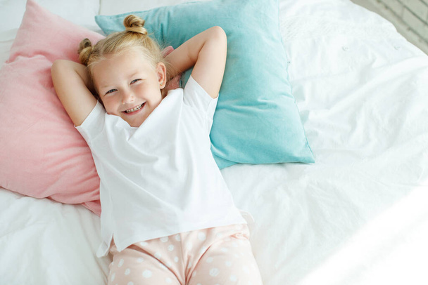 Beyaz çarşaflarla yatakta küçük bir kız. Sabah evde bir çocuk uyanır odasında.. - Fotoğraf, Görsel