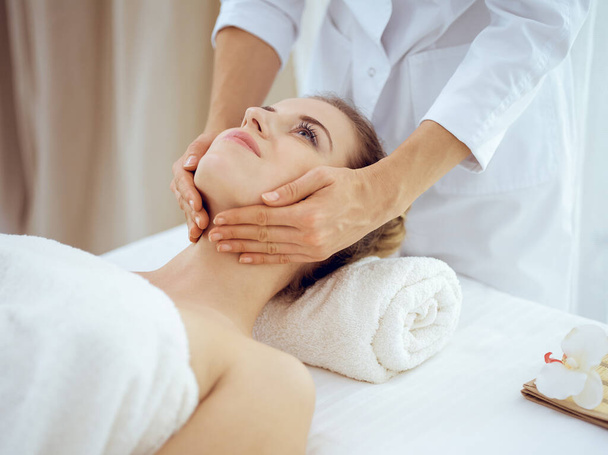 Young and blonde woman enjoying facial massage in spa salon. Beauty concept - Fotoğraf, Görsel