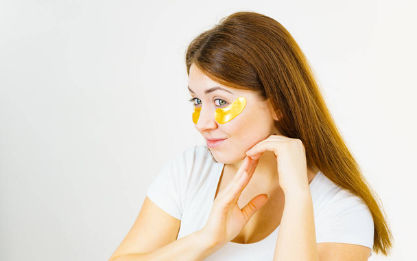 Young woman with golden collagen patches, under eye pads. Mask removing wrinkles and dark circles. Girl taking care of delicate skin around eyes. Beauty treatment. - Photo, Image