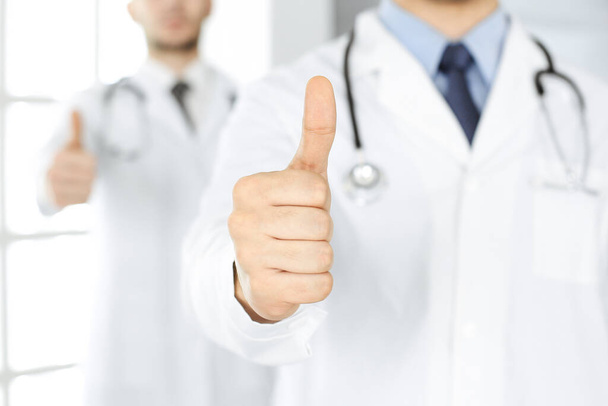 Two male doctors standing as a team with thumbs up in hospital office and ready to help patients. Medical help, best disease treatment and medicine concept - Zdjęcie, obraz