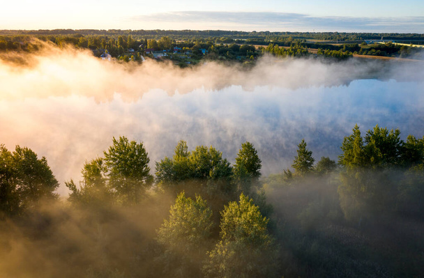 早朝の風景。フォギー川だ。日の出の朝の霧の中で川の谷。上からの眺め。木々の上の霧を突き抜ける太陽の光 - 写真・画像