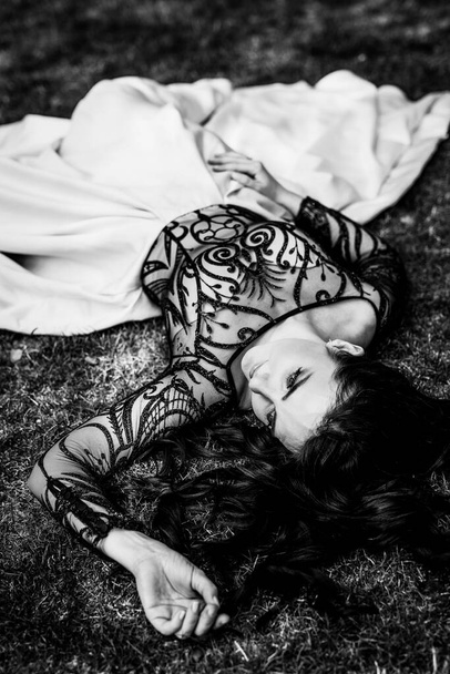 Hermosa mujer atractiva en vestido blanco negro y mirar hacia otro lado. Foto en blanco y negro de una joven tumbada sobre hierba verde - Foto, imagen