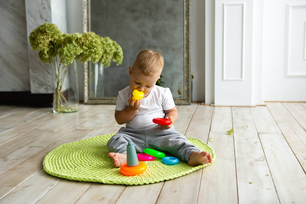Little child boy plaing with toy pyramid on knitted carpeet on the wooden floor indoor. Knitted style in the interior. Warm and cozy. Playful children. - Fotoğraf, Görsel