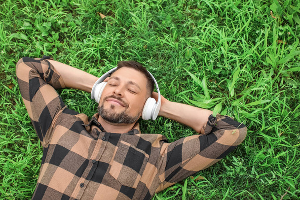 Knappe man die naar muziek luistert terwijl hij ontspant in het park - Foto, afbeelding