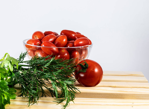 Bright red juicy tomatoes on a wooden stand in a glass bowl. A sprig of dill and parsley. - Φωτογραφία, εικόνα