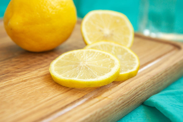 Limón y rodajas de limón amarillo se encuentran en una tabla de cortar de madera sobre un fondo de tela turquesa. Frutas tropicales. Cítricos frescos. Espacio libre para texto. Vista superior - Foto, Imagen