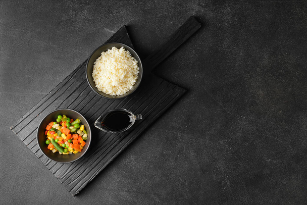 Bowls with tasty rice and vegetables on dark background - Φωτογραφία, εικόνα