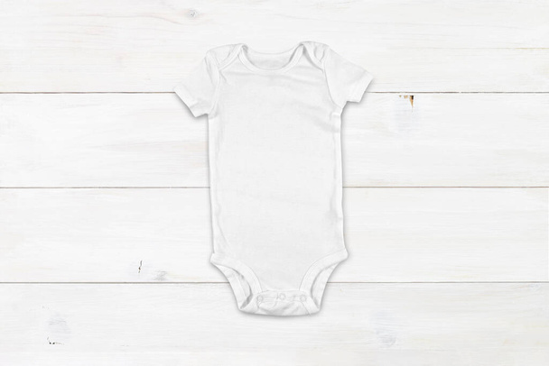 Top down view of a white onesie on a modern white wood background. Plenty of space to add your own design to the baby bodysuit. - Photo, Image