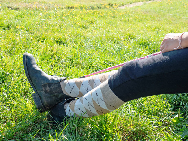 As pernas cruzadas usam botas de piquete e meias compridas no joelho. Cavaleiro segurar wisp enquanto sentar no paddock do clube de equitação.  - Foto, Imagem