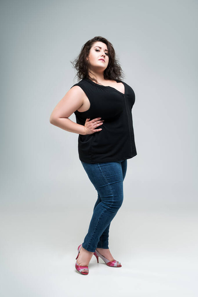 Plus size fashion model in black blouse and blue jeans, fat woman on gray studio background, body positive concept - Foto, Bild