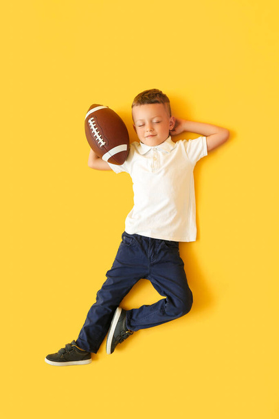Niño pequeño con pelota de rugby en el fondo de color, vista superior - Foto, Imagen