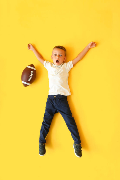 Kleiner Junge mit Rugby-Ball auf farbigem Hintergrund, Draufsicht - Foto, Bild