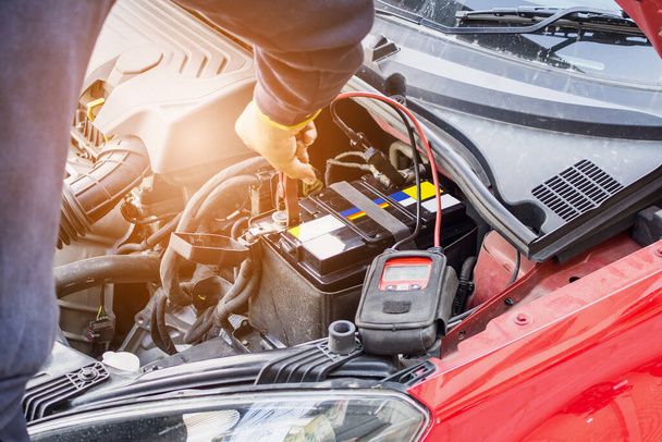 車の整備士は電圧計を使ってバッテリーの電圧レベルを確認します - 写真・画像