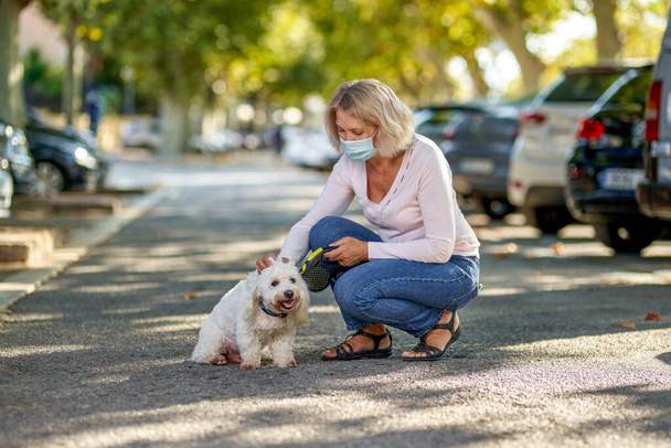外で犬と一緒に歩く高齢女性ウイルス対策マスク. - 写真・画像