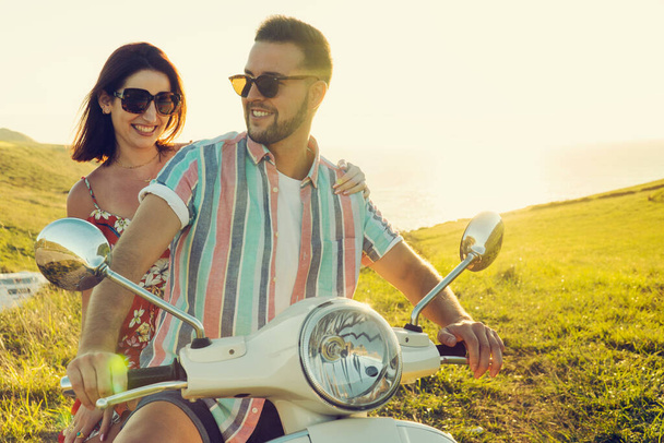 Pár fiatal barát friss ruhákkal, szórakozás és mosolygás egy motorkerékpáron a parton a naplemente fényénél - Fotó, kép