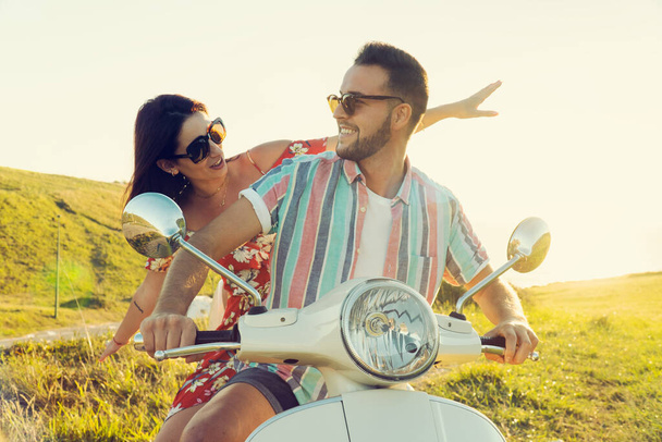 Kilku młodych przyjaciół ze świeżymi ubraniami, bawiących się i uśmiechających na motocyklu na wybrzeżu w świetle zachodu słońca - Zdjęcie, obraz