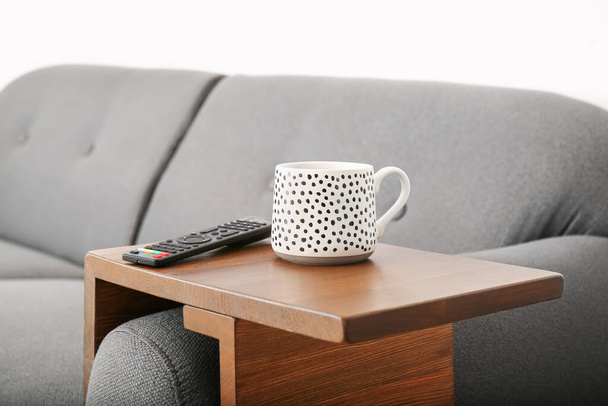 Cup of tea with remote control on armrest table in room - Photo, Image