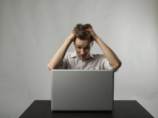 Frustrated young man with laptop. Man in white is suffering from headache. Expressions, feelings and moods. - Foto, Imagen