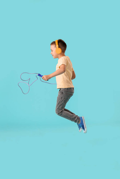 Симпатичный маленький мальчик в наушниках прыгает канат на цветном фоне - Фото, изображение