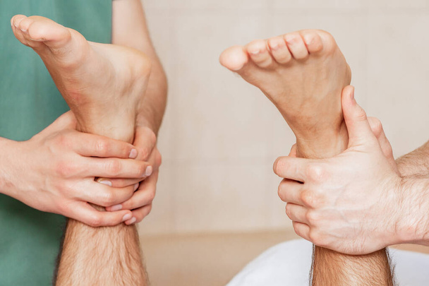 Κοντινό πλάνο των χεριών δύο θεραπευτών μασάζ μασάζ πόδια του ανθρώπου στο σαλόνι μασάζ. - Φωτογραφία, εικόνα