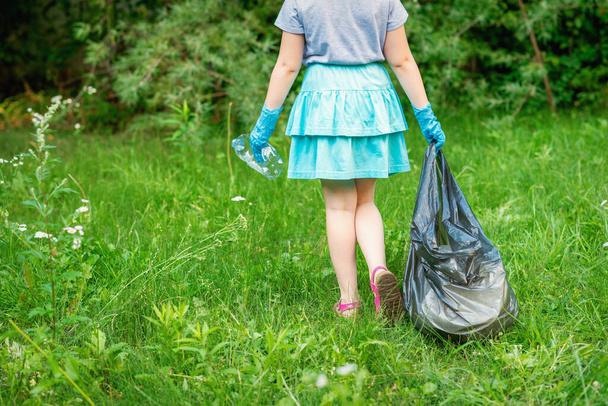 Маленькая девочка чистит пластиковый мусор на зеленой траве в парке - Фото, изображение