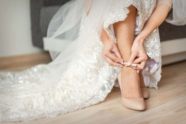 Bride puts on wedding shoes on her feet wearing beautiful wedding dress - 写真・画像