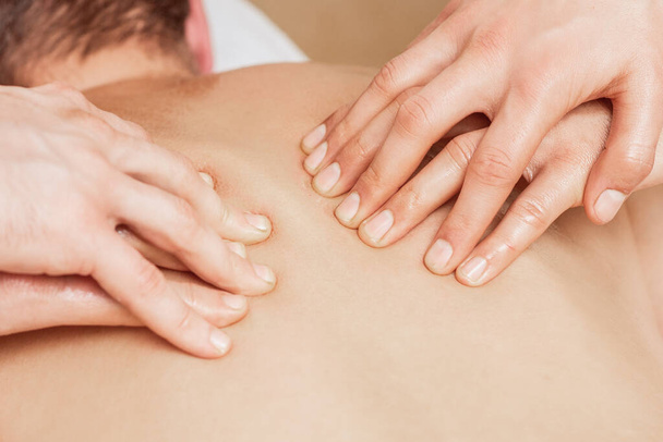 Hombre recibiendo masaje de espalda en cuatro manos de dos terapeutas masculinos de cerca. - Foto, Imagen